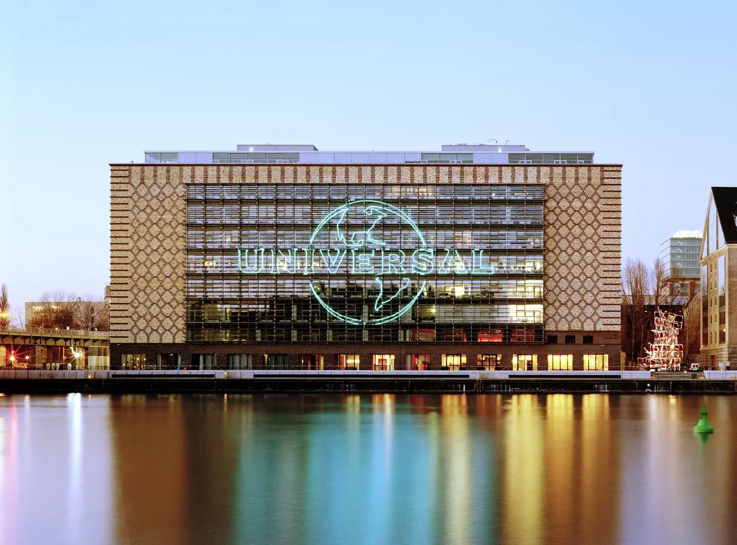 Hauptsitz der Universal Music Group in Berlin am Wasser mit beleuchtetem grünen Logo an der Glasfassade